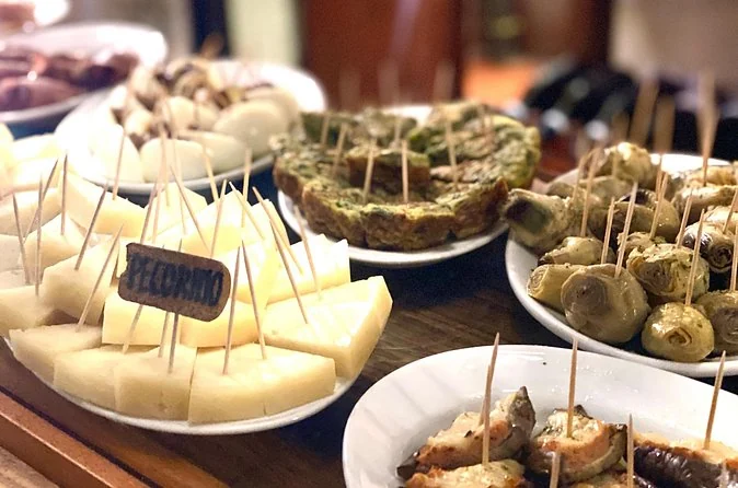 Plates of cicchetti on a bar counter: cheese, stuffed vegetables and small skewers with handwritten labels
