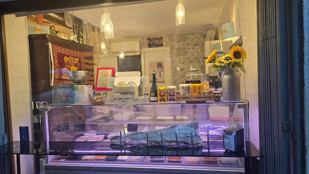 The glass counter of a small Venetian bar lit warmly, with bottles and plates behind it